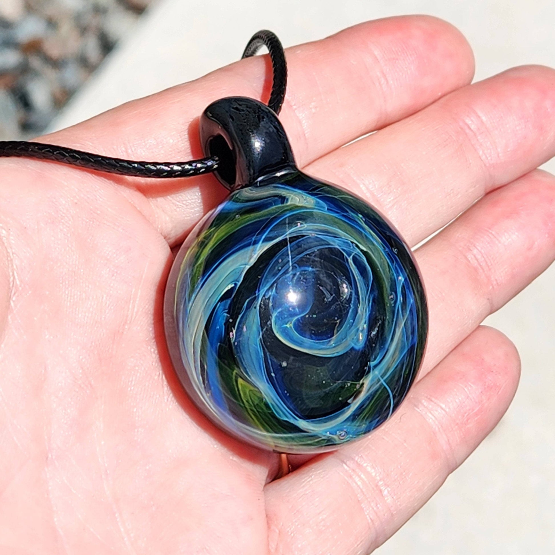 Close-up of Heady Glass Pendant in hand, featuring a vivid galaxy swirl in blue, green, and gold, crafted from borosilicate glass.