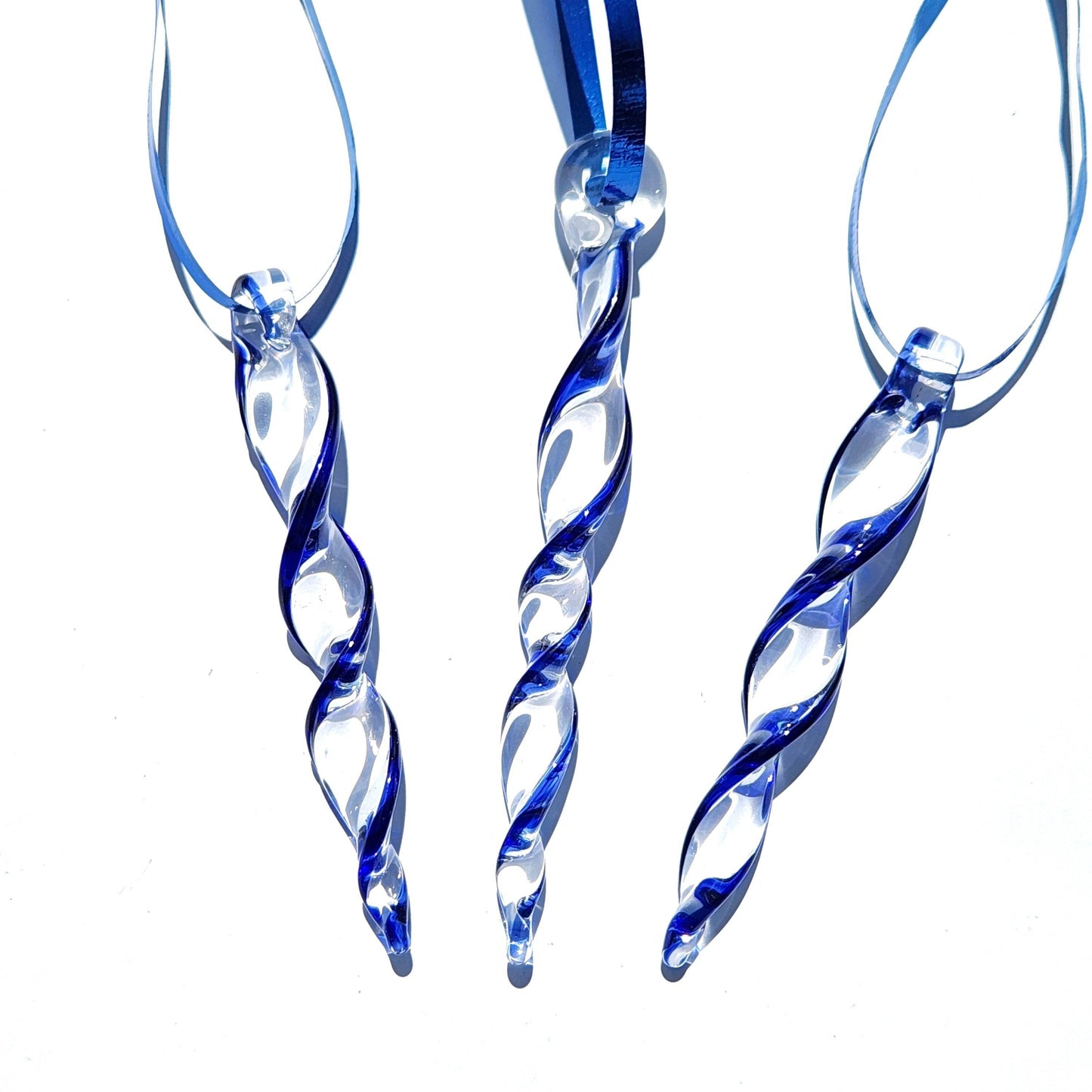 Three blue glass icicle ornaments with blue ribbons on white background, ideal handmade Christmas decorations or suncatchers.