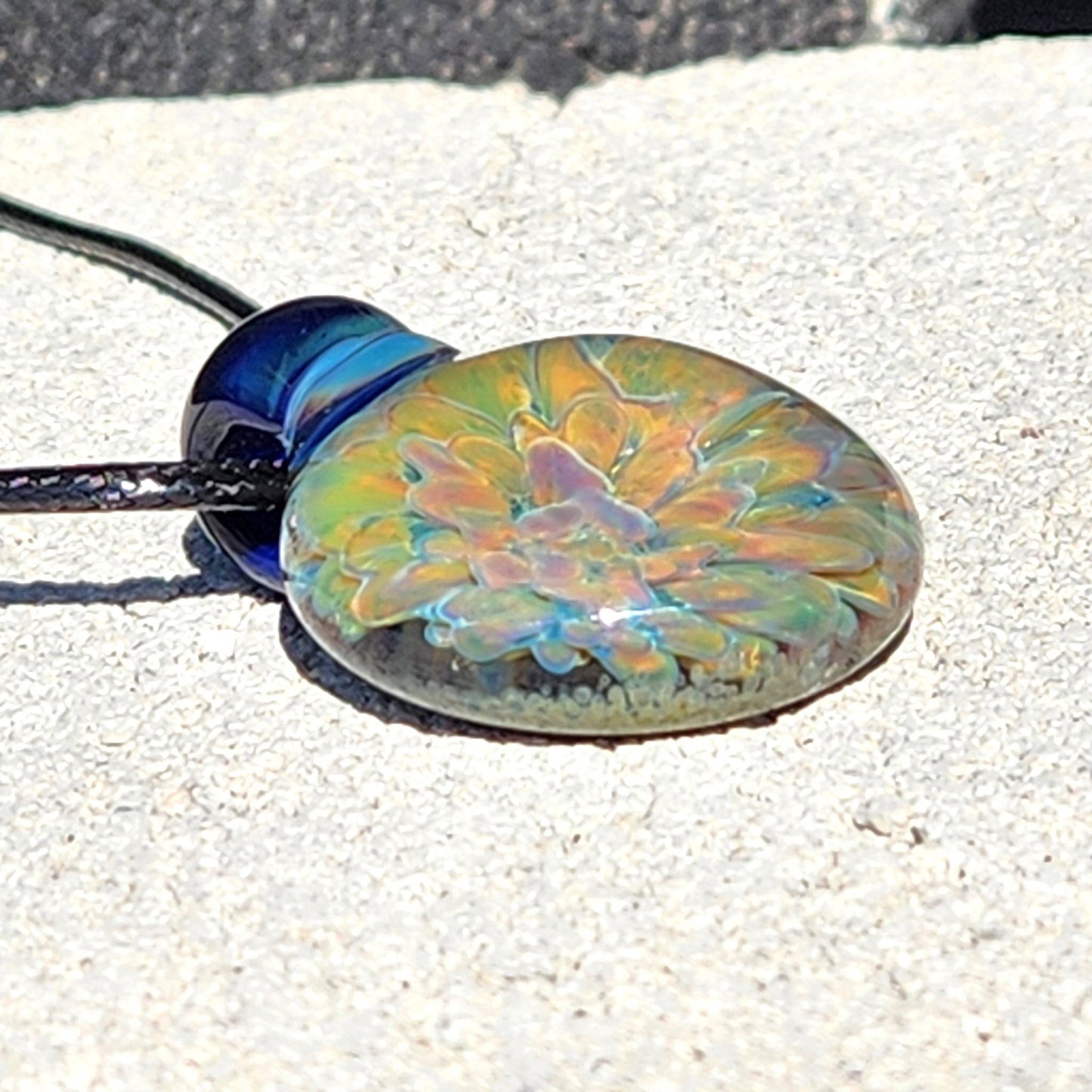 Unique glass pendant necklace with iridescent flower design, shown from a side angle to highlight its domed shape.