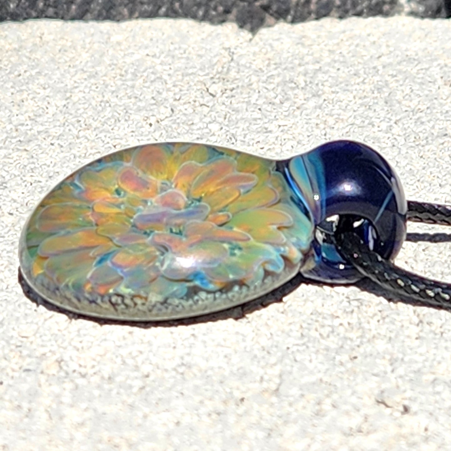 Close-up of handmade glass pendant necklace with rainbow-hued flower design, lying flat on a light surface.