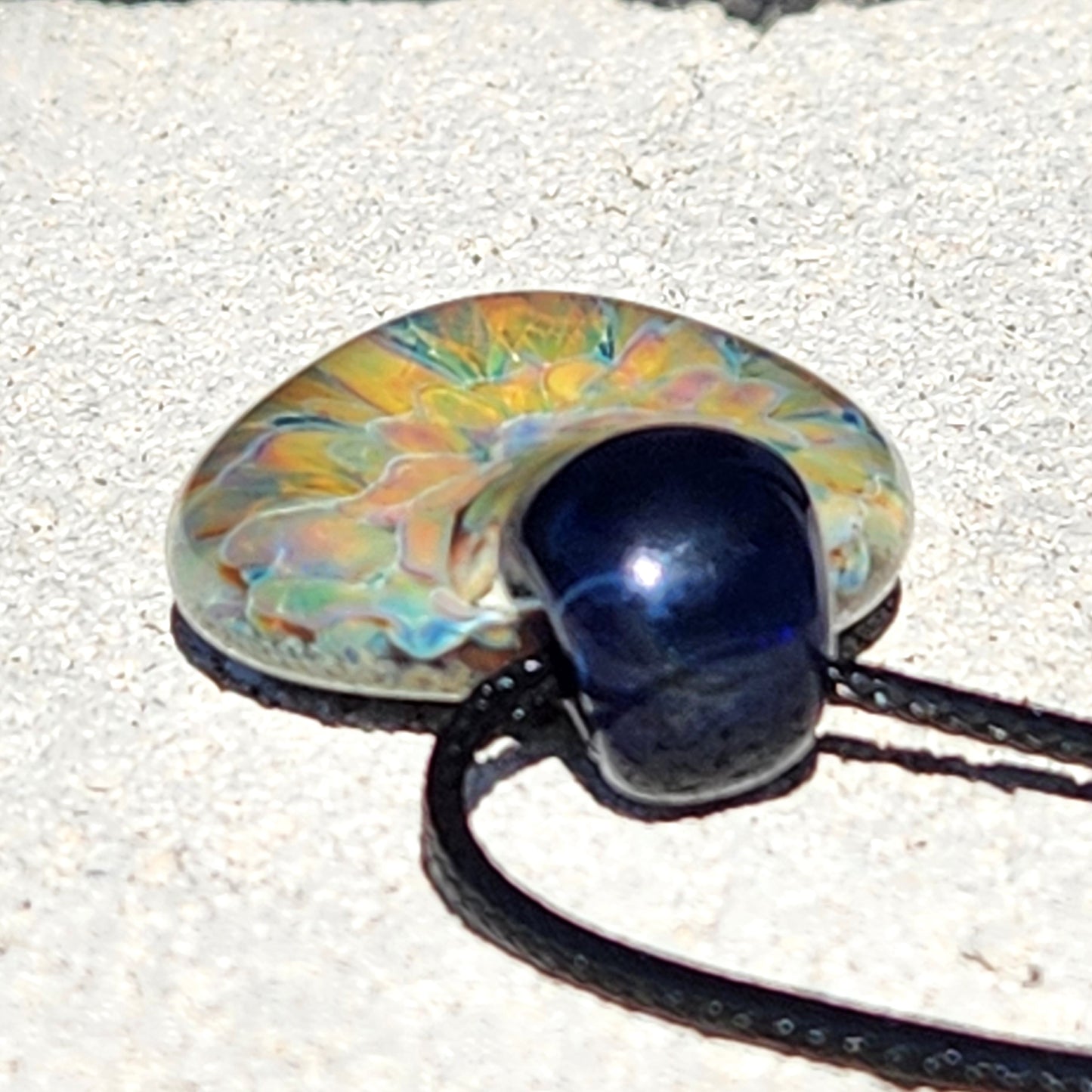 Side view of trippy glass pendant necklace showing its curved shape and detailed flower design with black cord.