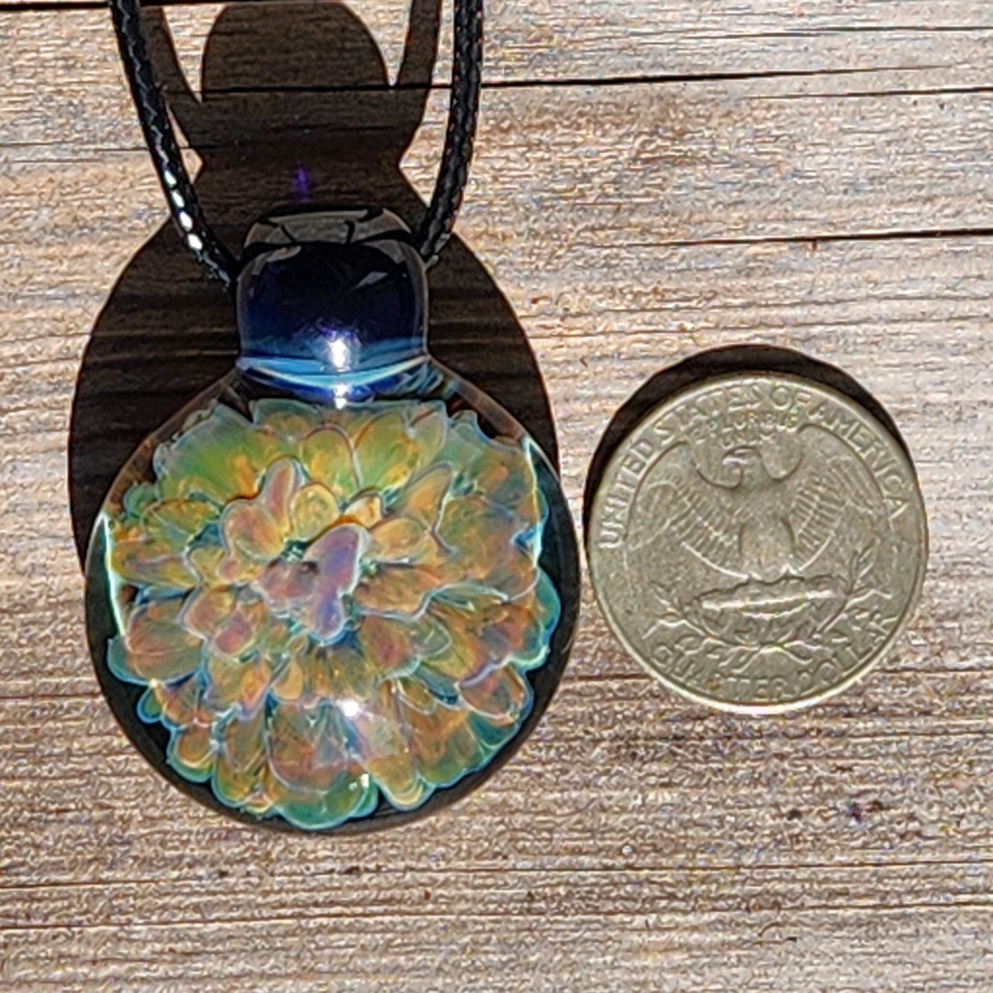 Handmade glass pendant necklace next to a US quarter for size comparison, featuring a colorful trippy flower design.