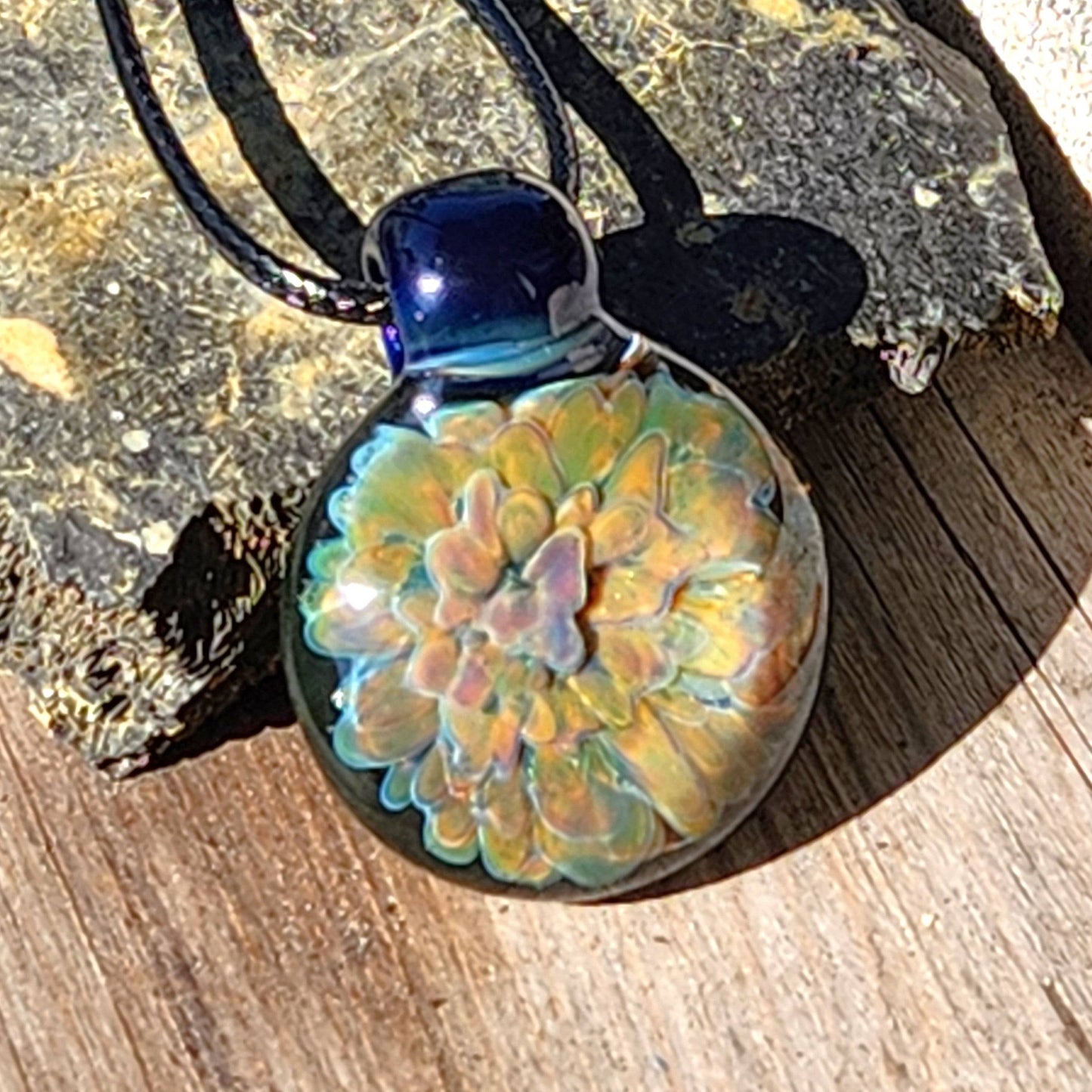 Handmade trippy jewelry pendant featuring a vibrant floral pattern in glass, displayed on a rustic stone background.