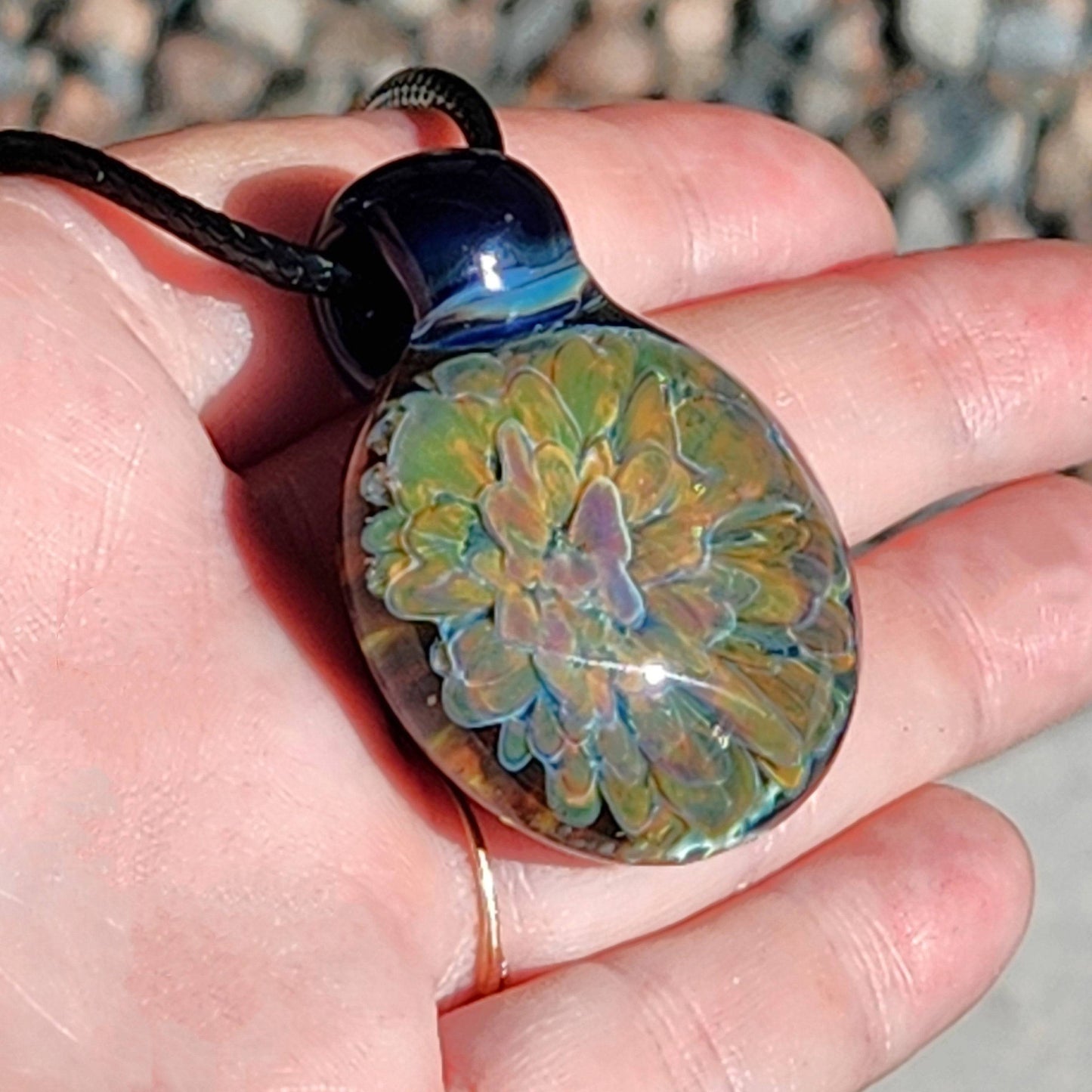 One-of-a-kind trippy glass pendant necklace held in hand, showcasing its vivid layered flower design and glossy surface.