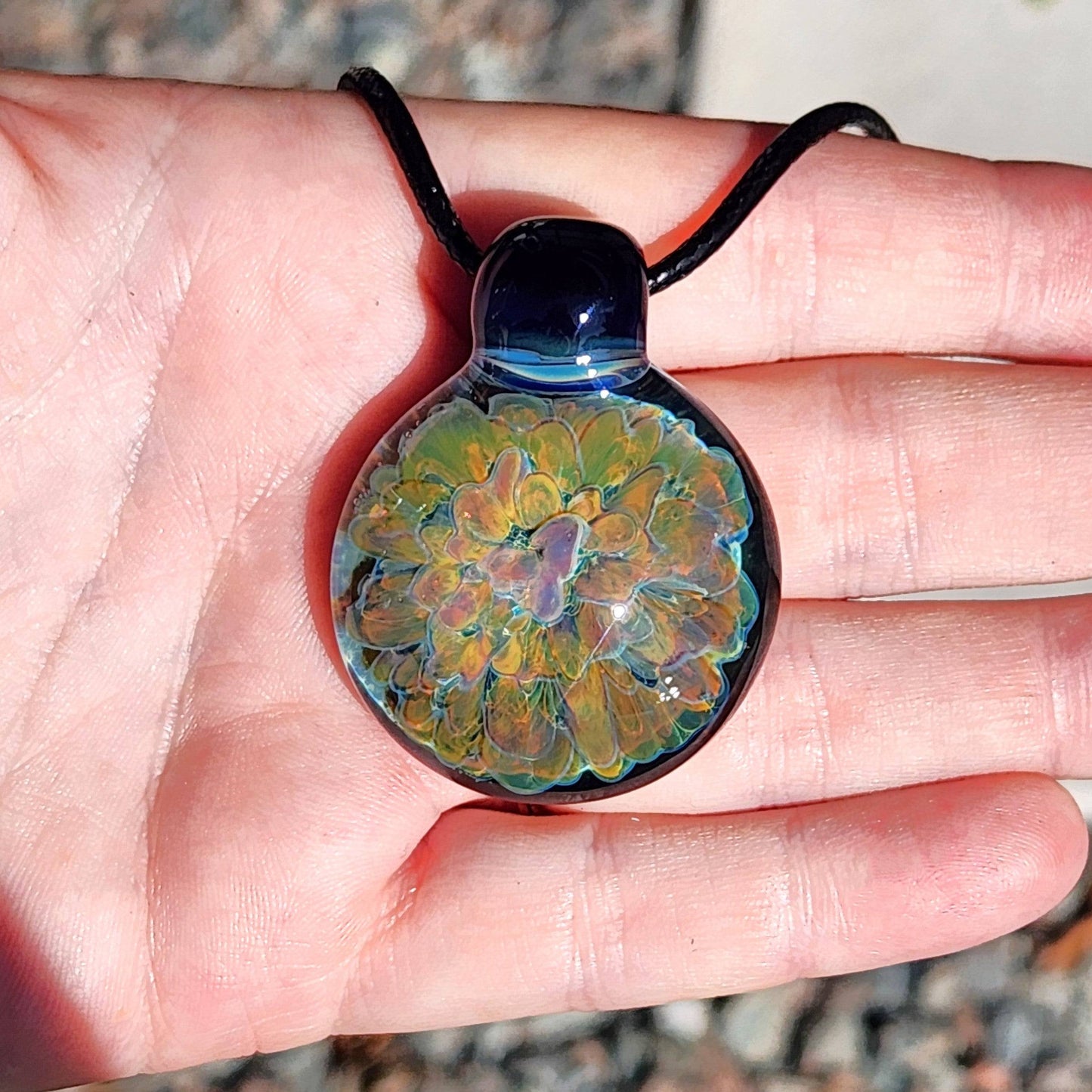 Glass pendant necklace with psychedelic floral design shown in hand, emphasizing its size and intricate craftsmanship.