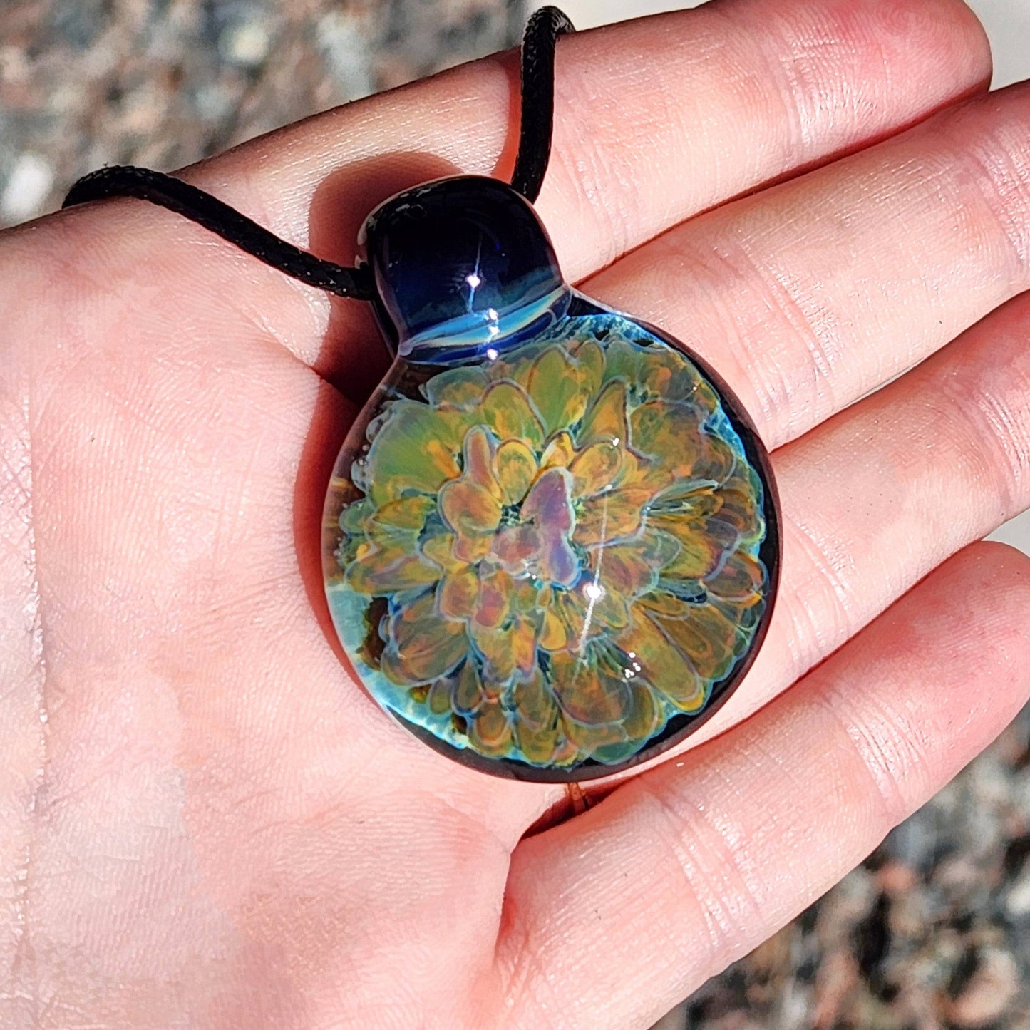 Unique handmade trippy jewelry pendant with vibrant flower encased in glass, displayed in natural sunlight on hand.