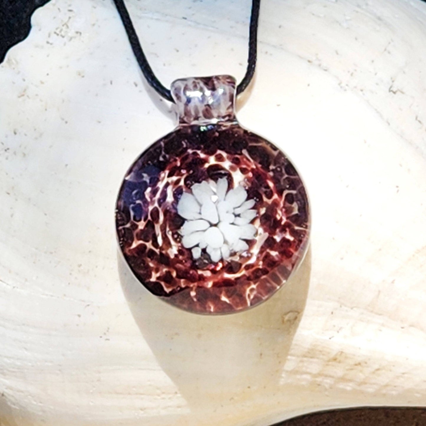 Handmade White and Black Glass Necklace featuring a white flower design in a speckled pendant, shown on a shell backdrop for jewelry display.