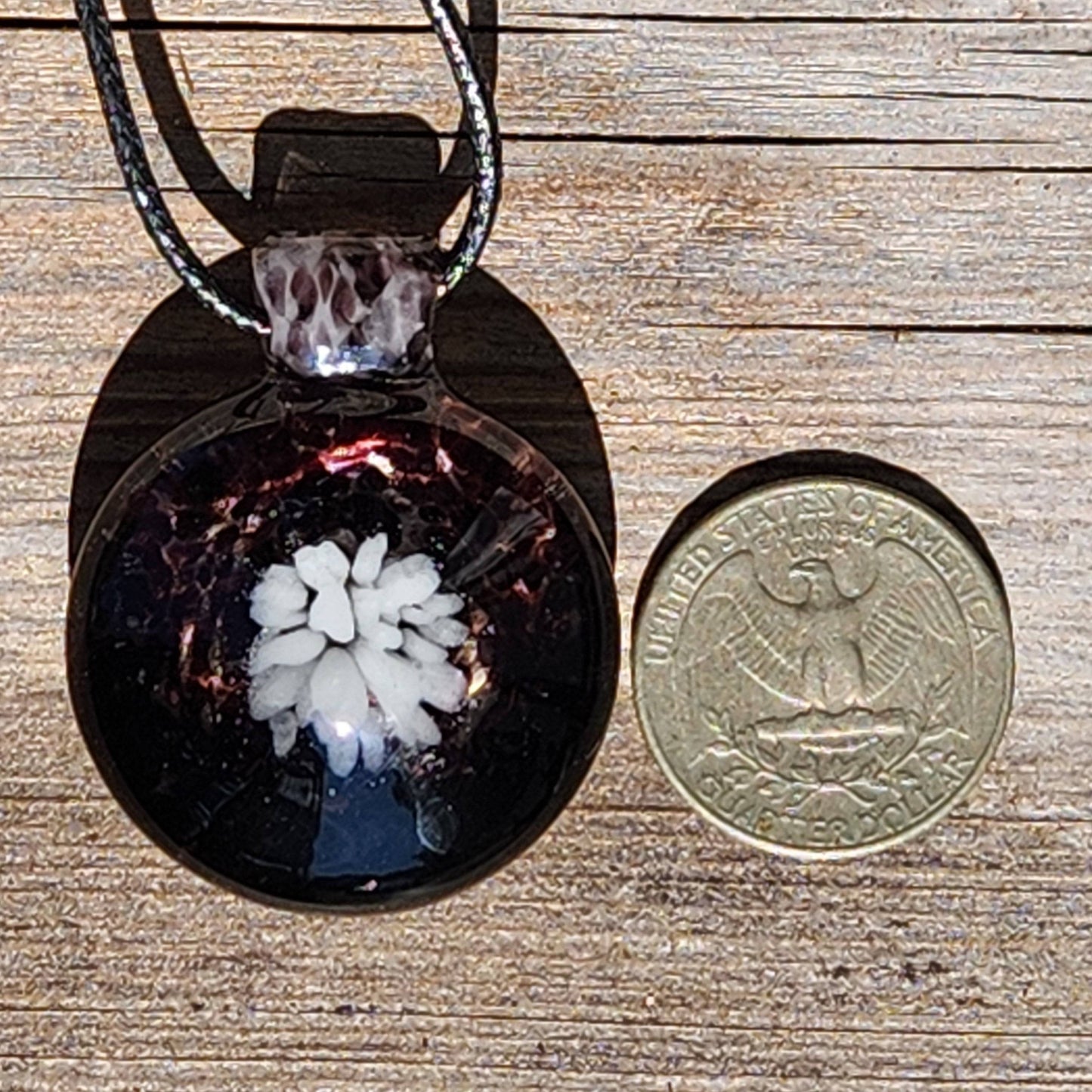 Heady Blown Glass Pendant next to a US quarter for size comparison, featuring white flower in black and white handmade glass necklace.