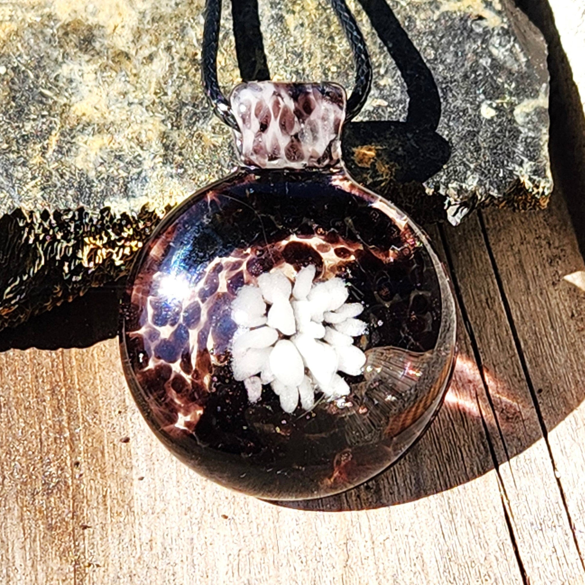 Handmade White and Black Glass Necklace pendant with white flower center and speckled glass, displayed on wood for rustic jewelry appeal.