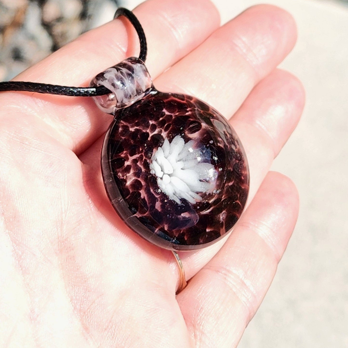Hand holding Handmade White and Black Glass Necklace pendant, highlighting size and intricate flower detail in borosilicate glass jewelry.