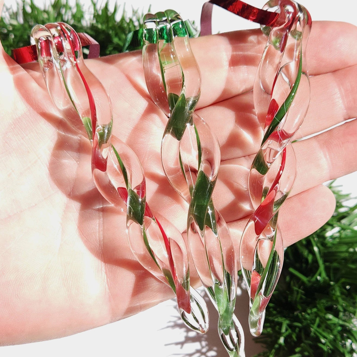 Hand holding three red and green twisted glass Christmas ornaments, showcasing the detailed craftsmanship of each custom icicle.