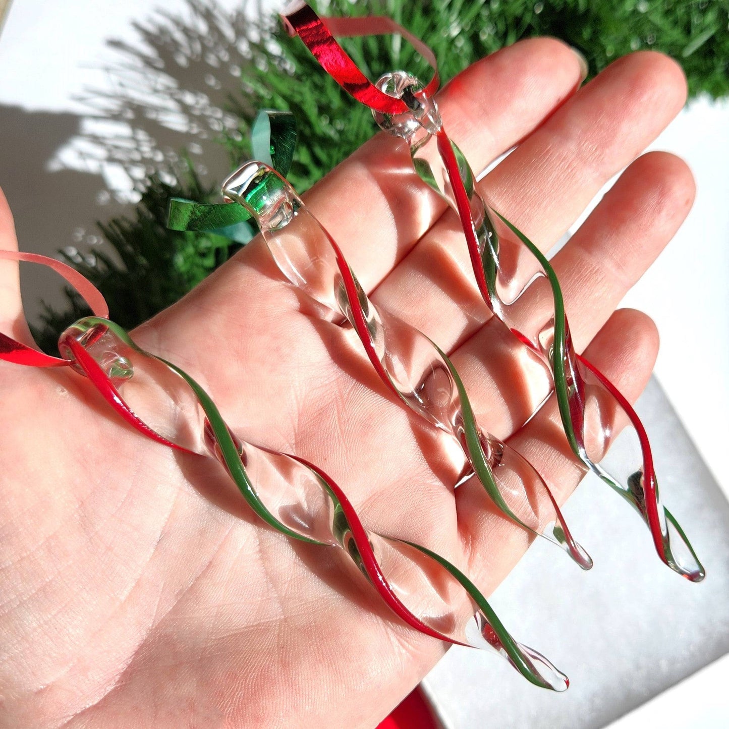Hand holding Unique Handmade Glass Icicle Ornaments - Festive 3-Piece Ornament Set, showing size and intricate red-green swirl craftsmanship.