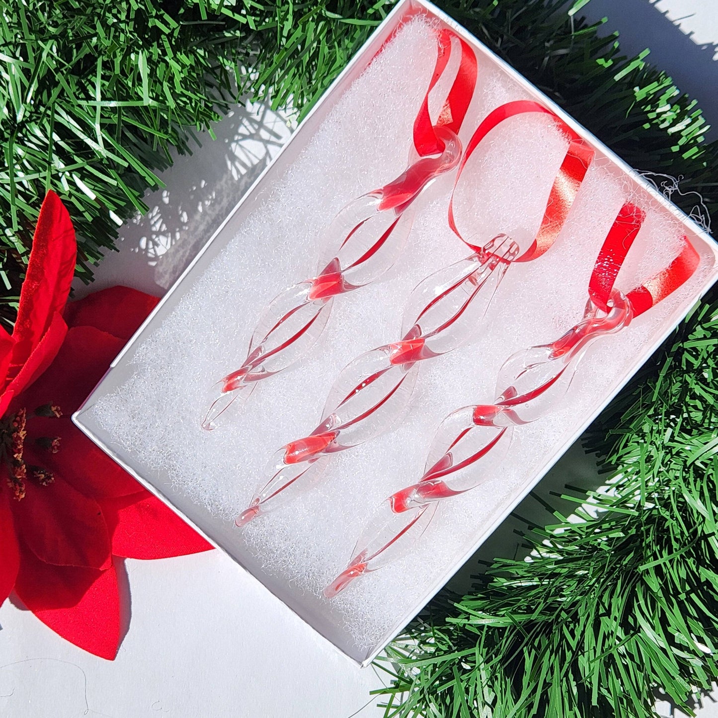 Box of three red handmade glass icicle ornaments with ribbon loops, ideal for Christmas tree decoration and seasonal gifts.