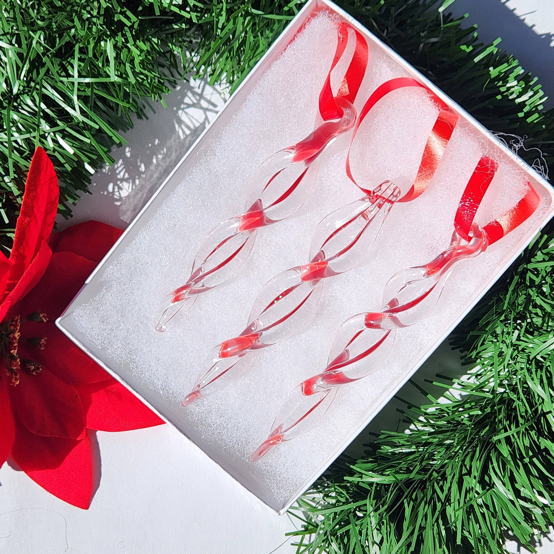 Box of three red handmade glass icicle ornaments with ribbon loops, ideal for Christmas tree decoration and seasonal gifts.