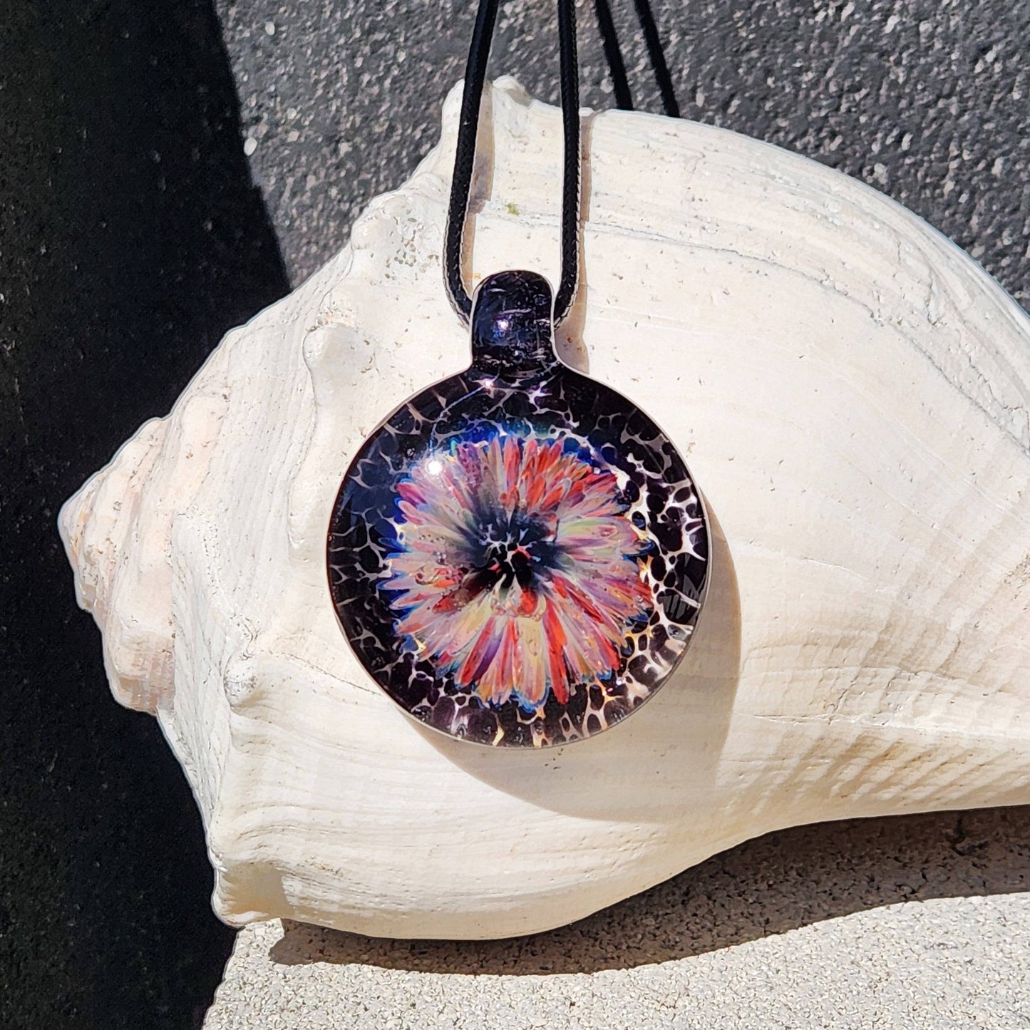 Handmade jewelry blown glass pendant necklace with a vivid flower design in purple, red, and cream on a black background. Unique borosilicate charm.