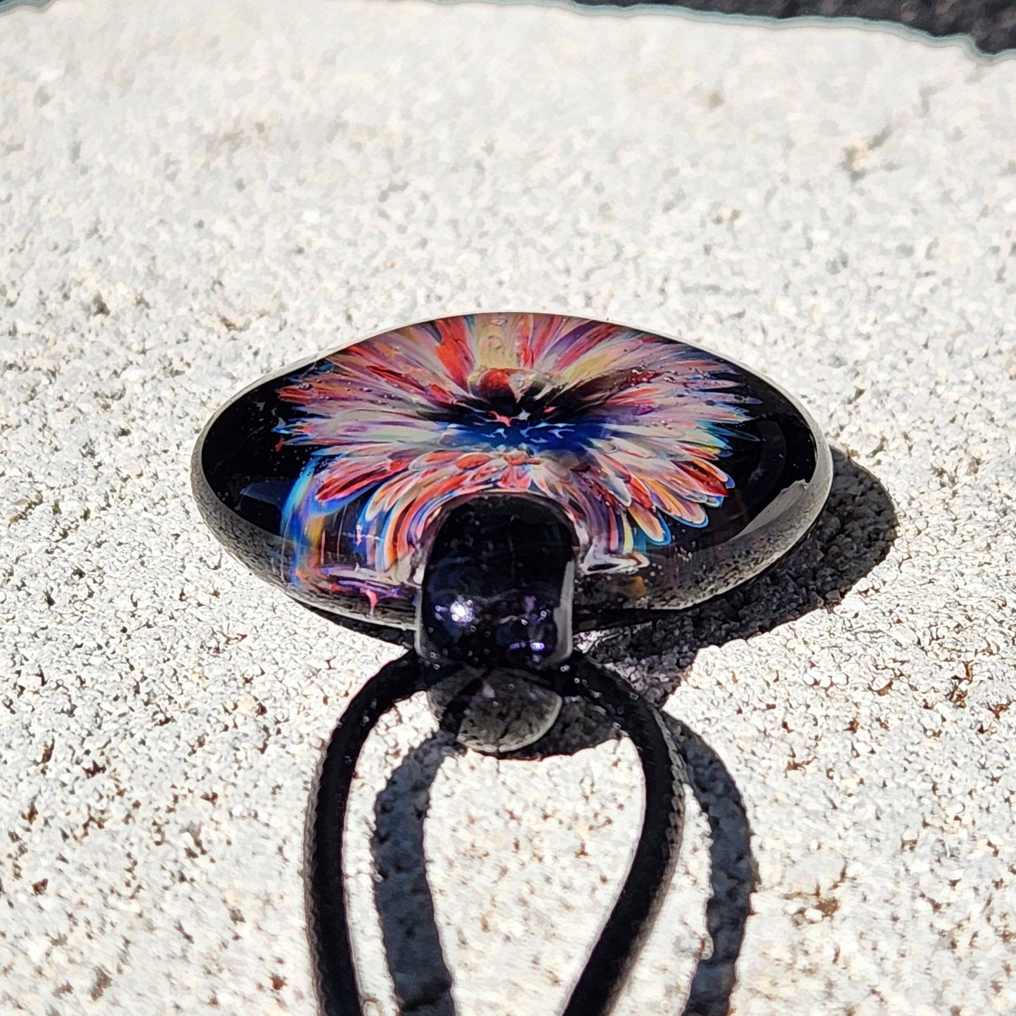 Side angle of a handmade borosilicate glass pendant with a radiant floral center in purple and red, perfect for unique jewelry collections.