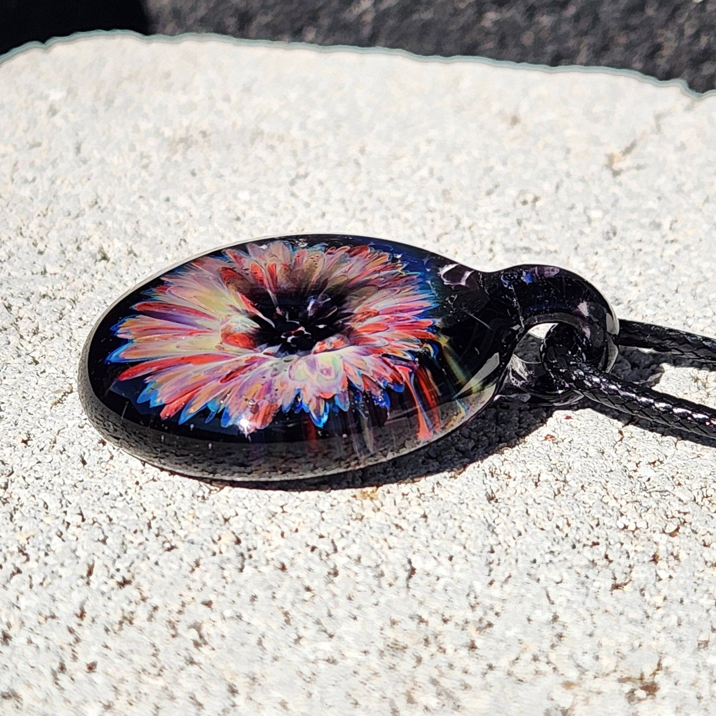 Detailed view of a handmade glass pendant necklace with a colorful flower encased in dark glass, ideal for gifting or personal style.