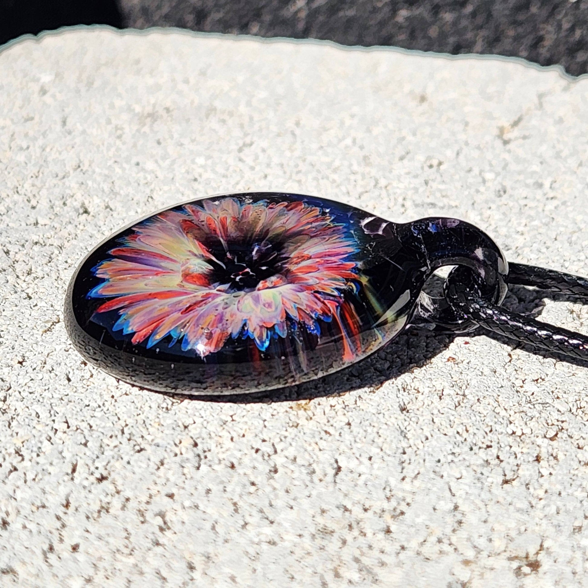 Detailed view of a handmade glass pendant necklace with a colorful flower encased in dark glass, ideal for gifting or personal style.