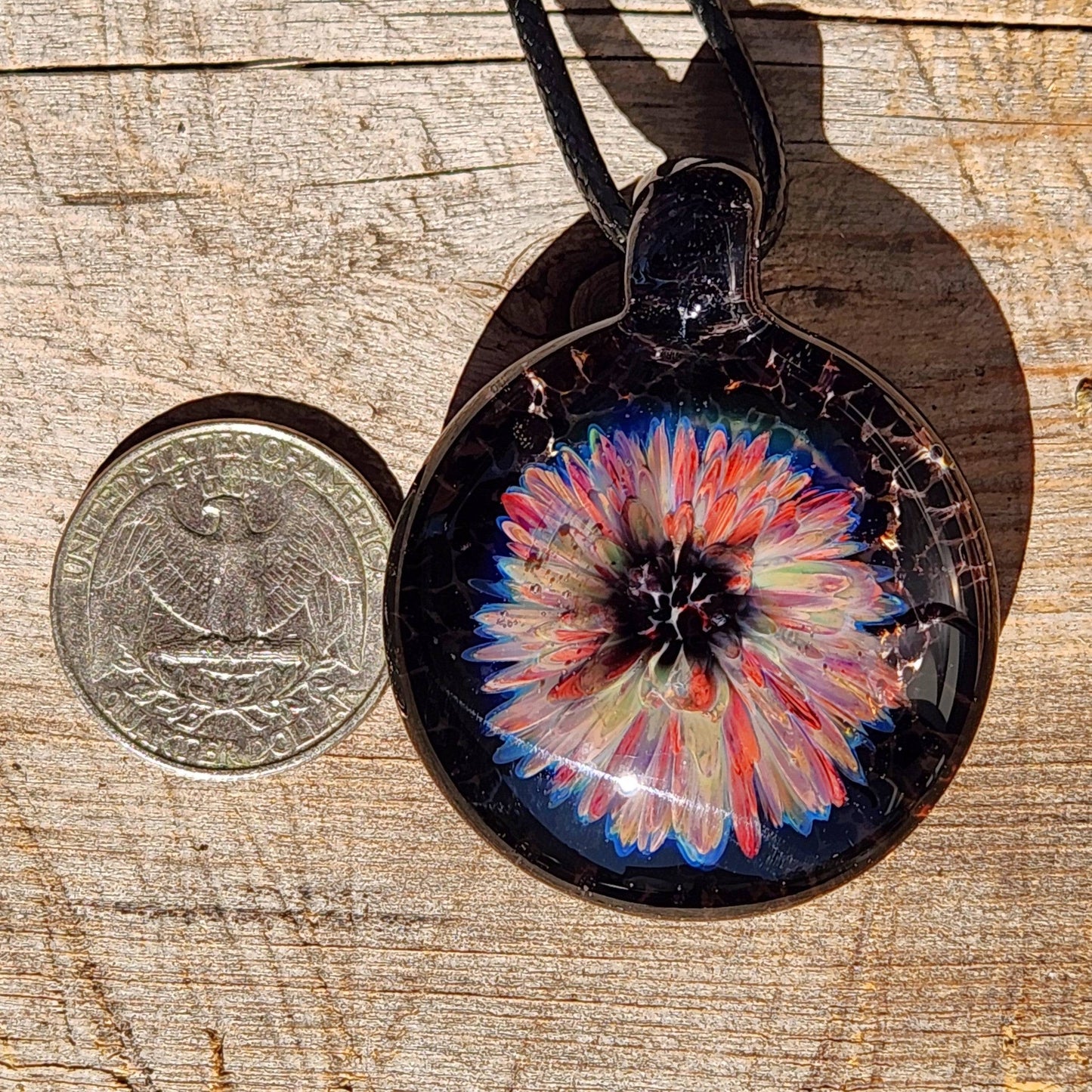 Size comparison of handmade blown glass flower pendant next to a US quarter, showcasing its compact and wearable design.