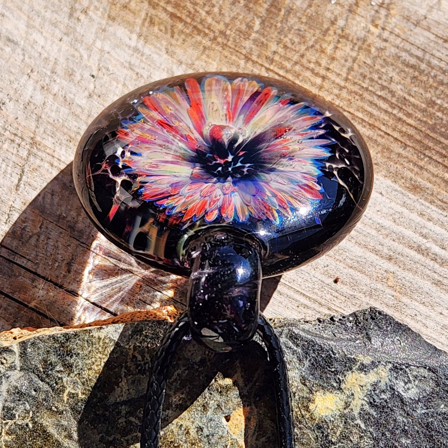 Close-up of handmade blown glass pendant with intricate flower pattern in purple and red tones, set against a black background. Artisan jewelry gift.