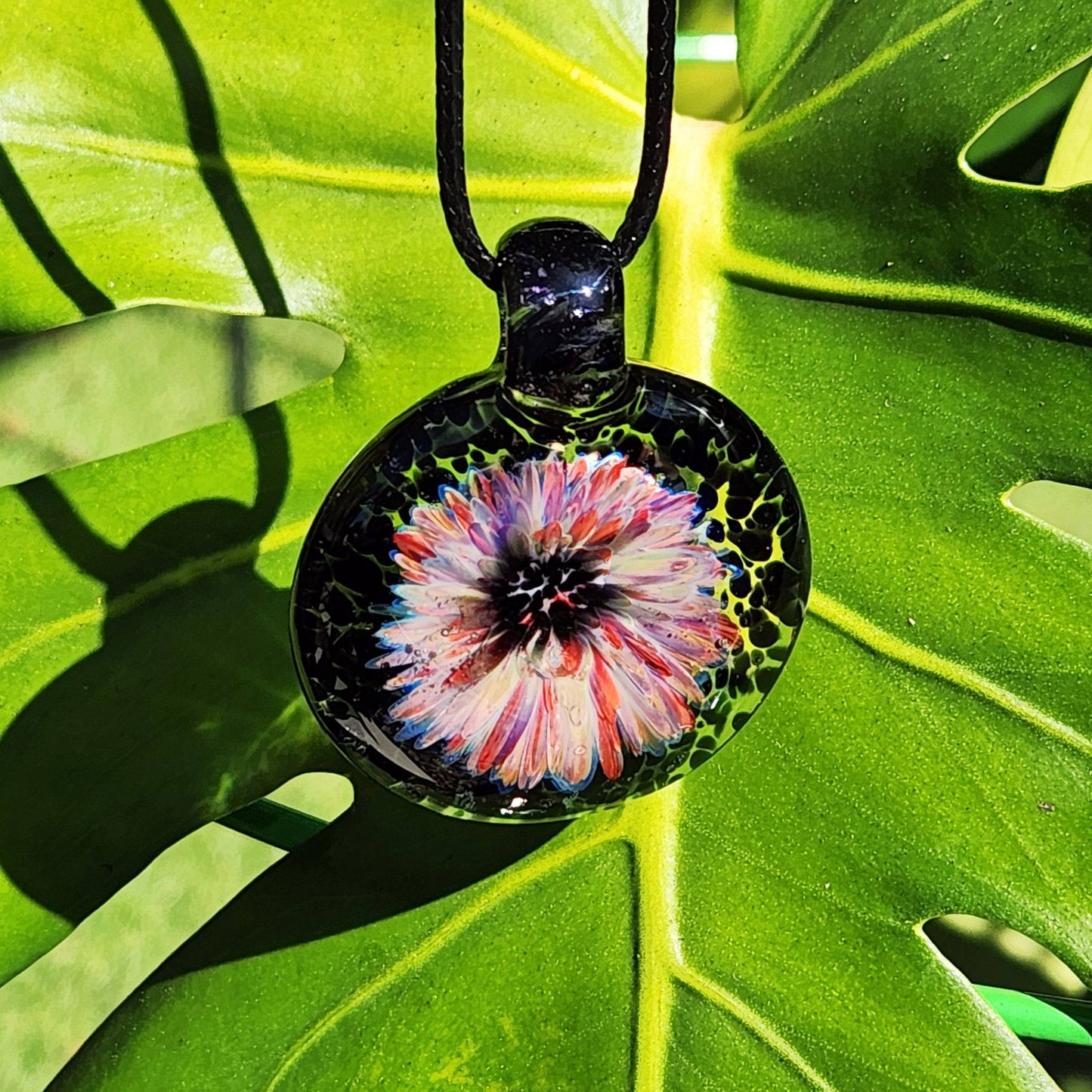 Handmade blown glass pendant necklace with a vivid flower design, displayed on a green leaf for a natural and vibrant jewelry presentation.