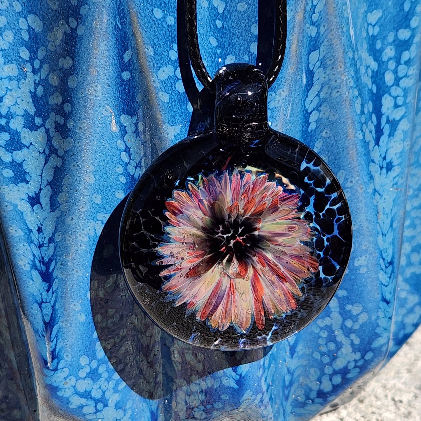 Colorful flower pendant necklace made from blown borosilicate glass, featuring purple and red petals on a dark background. Handmade jewelry charm.