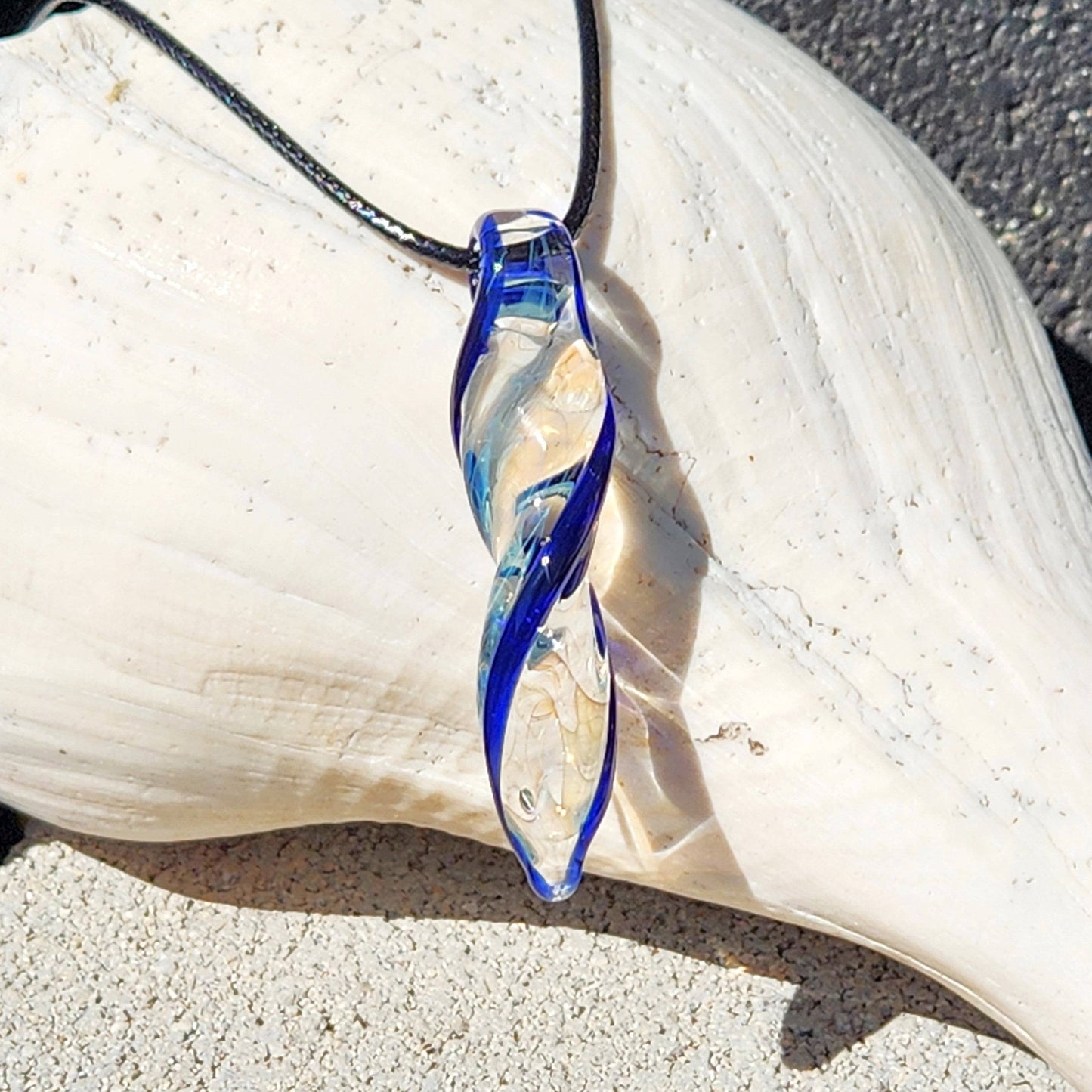 Silver-fumed Blown Glass Spiral Pendant with blue highlights, handcrafted and suspended on black cord, resting on white shell.