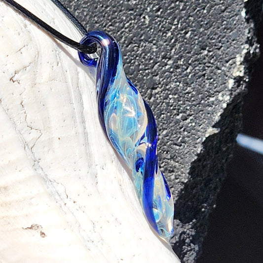 Blown Glass Spiral Pendant with silver-fumed swirl and blue accents, handmade jewelry charm on black cord, displayed on shell.