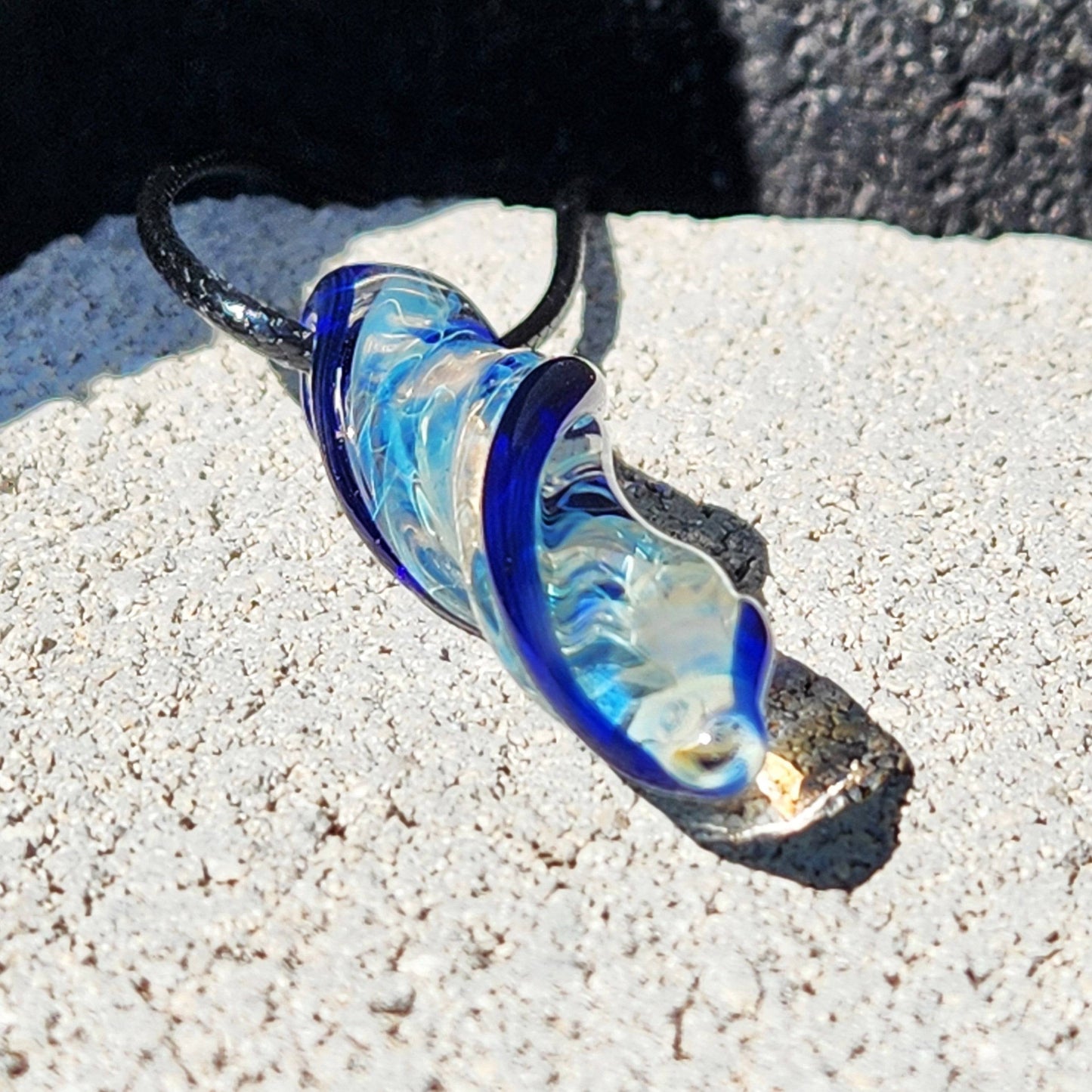 Elegant Blown Glass Spiral Pendant with silver-fumed and blue swirl design, resting on light stone surface in natural light.