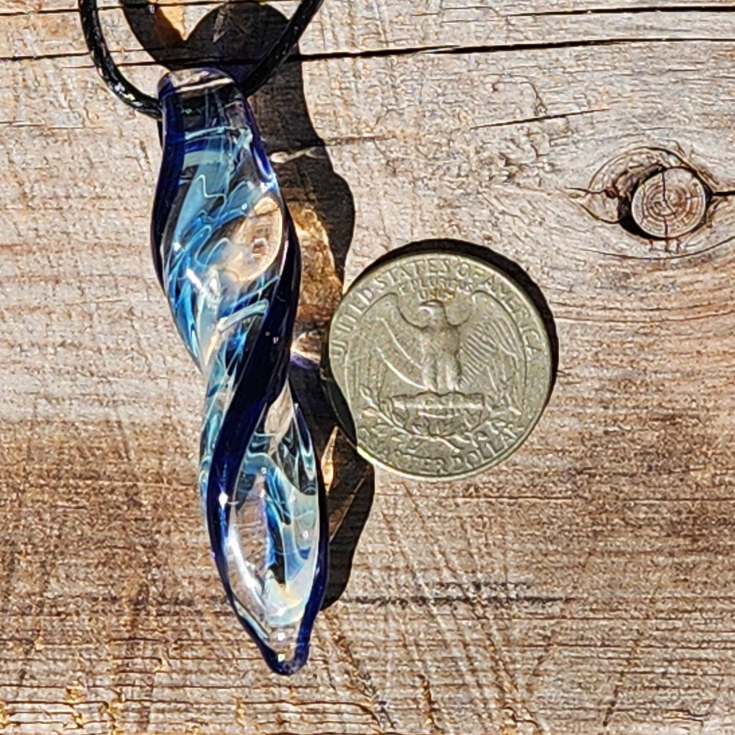 Size comparison of Blown Glass Spiral Pendant with silver-fumed blue swirl next to US quarter on wooden surface.