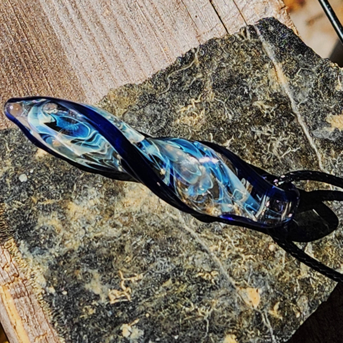 Artisan Blown Glass Spiral Pendant with silver-fumed swirl and deep blue accents, displayed on rustic stone background.