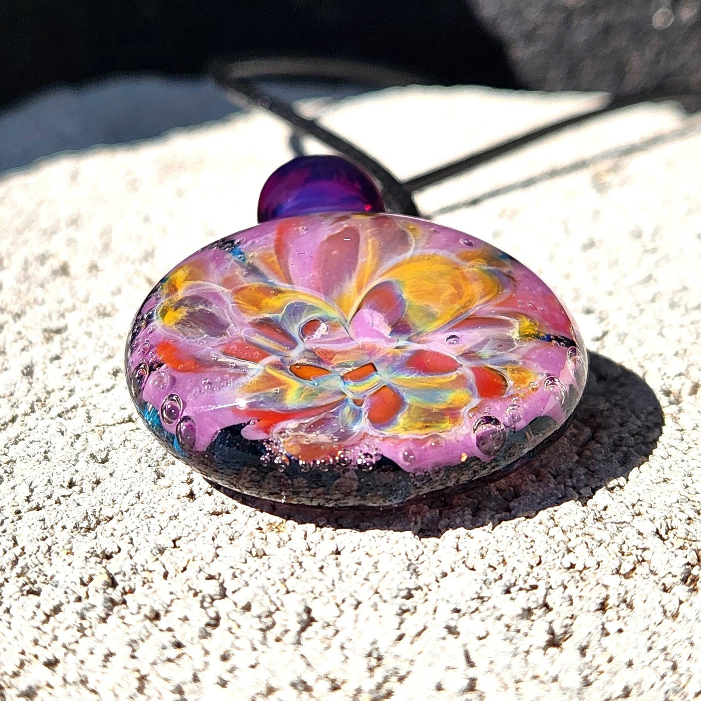 A handblown multicolored glass pendant with a floral pattern, attached to a black cord