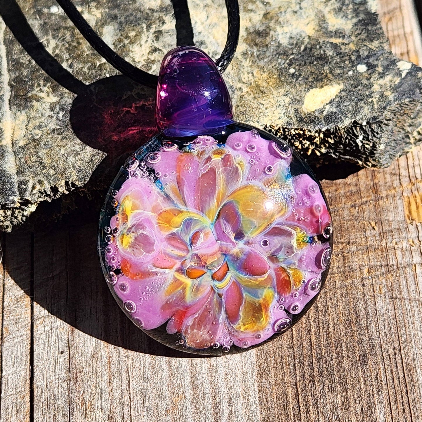 A handblown multicolored glass pendant with a floral pattern, attached to a black cord