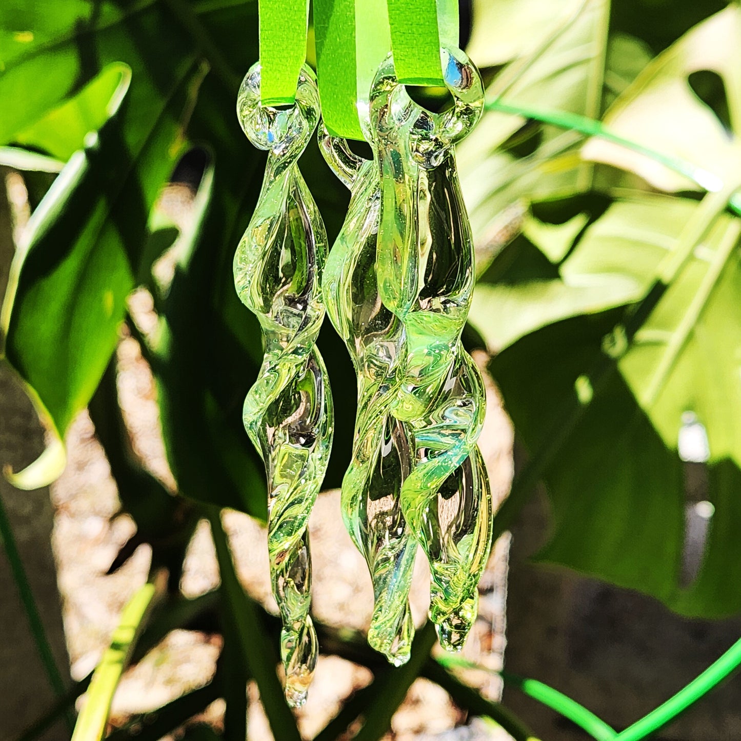Close-up of 3 lime green spiral glass suncatchers hanging outdoors, reflecting sunlight and enhancing garden ambiance.