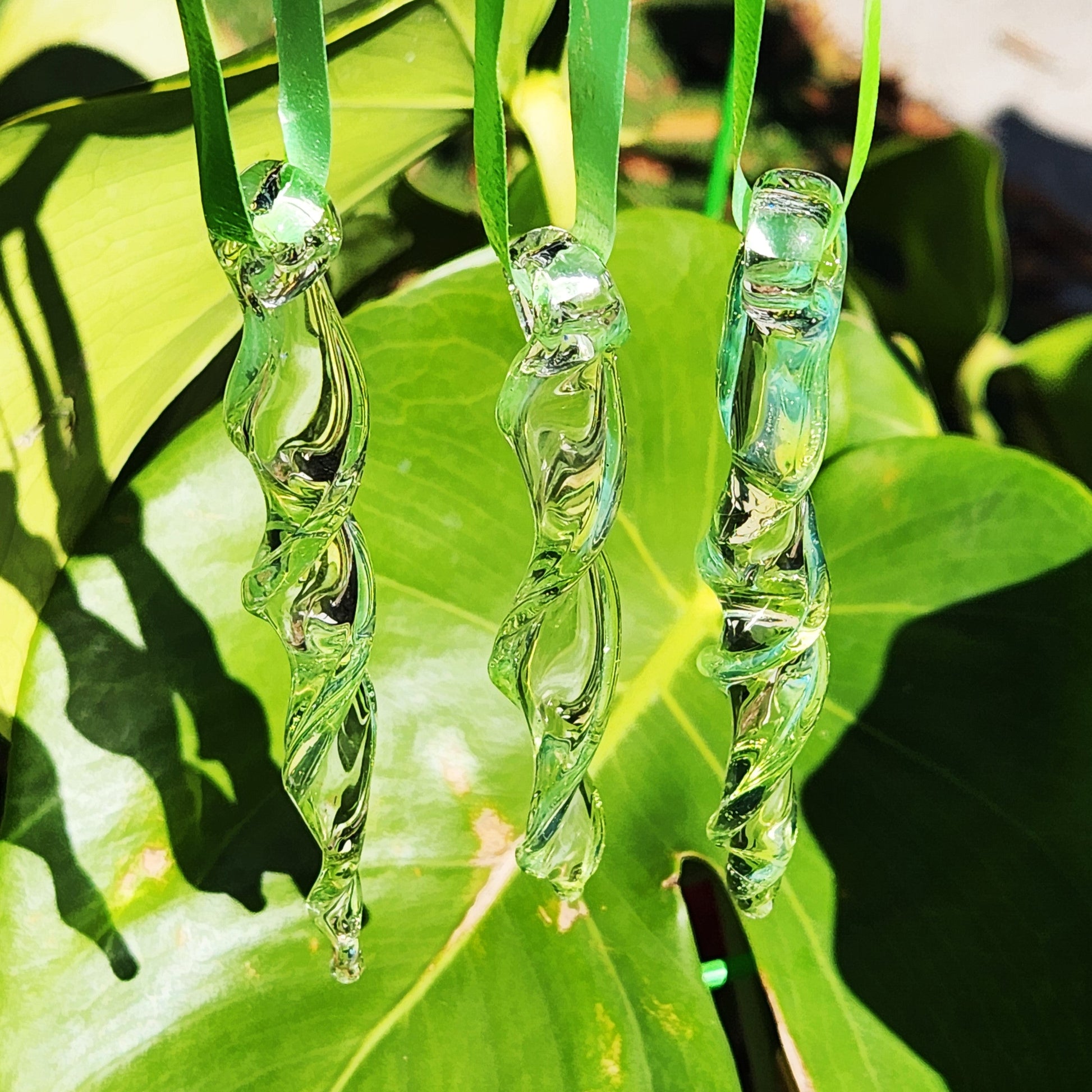 Three lime green spiral glass suncatchers hanging in front of tropical leaves, perfect for handmade garden art and outdoor decor.