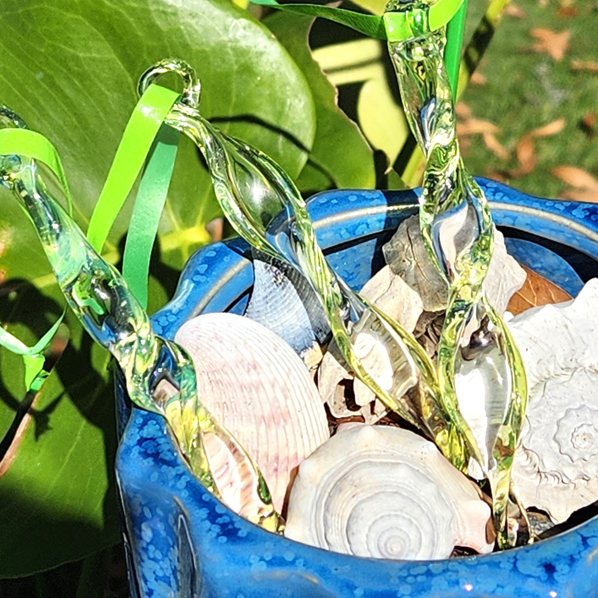 Lime green spiral glass suncatchers displayed in a blue pot with seashells, ideal for enhancing garden or patio decor.