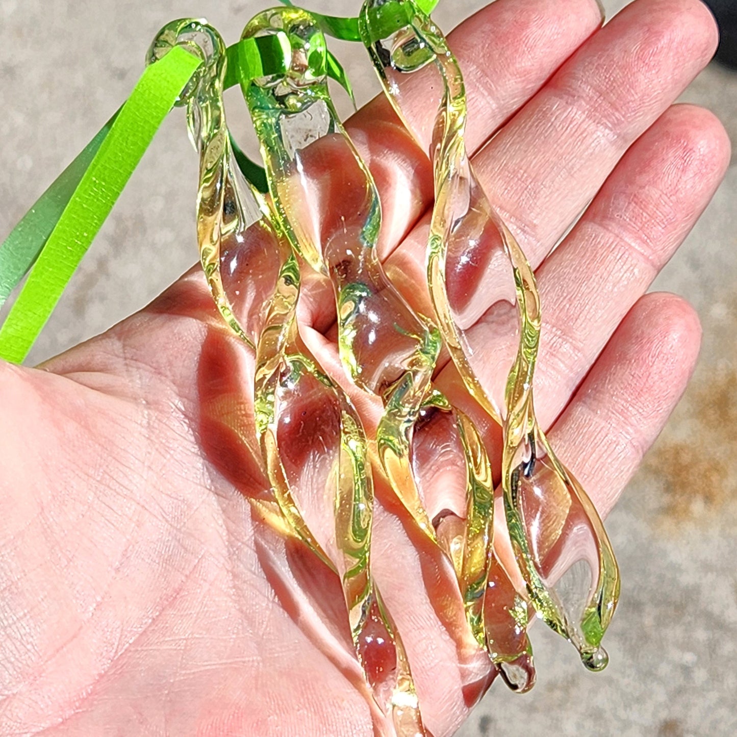Hand holding a set of 3 lime green spiral glass suncatchers with green ribbons, showcasing their size and intricate twisted design.