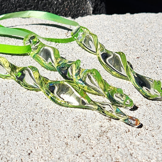 Set of 3 lime green spiral glass suncatchers handmade from borosilicate glass, displayed on a stone surface with bright sunlight reflections.
