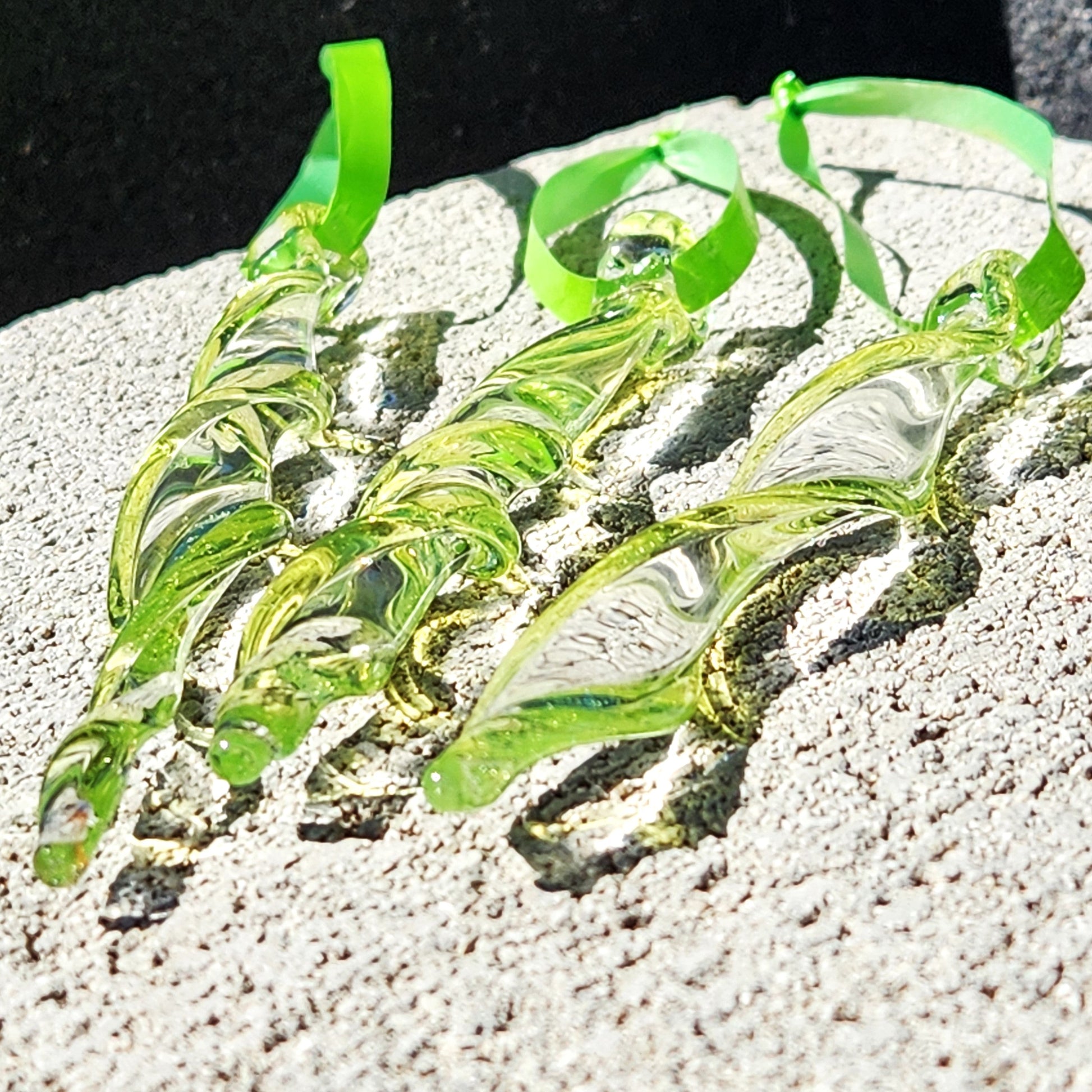 Trio of lime green spiral glass suncatchers resting on a textured stone surface, highlighting their handmade twisted glass design.