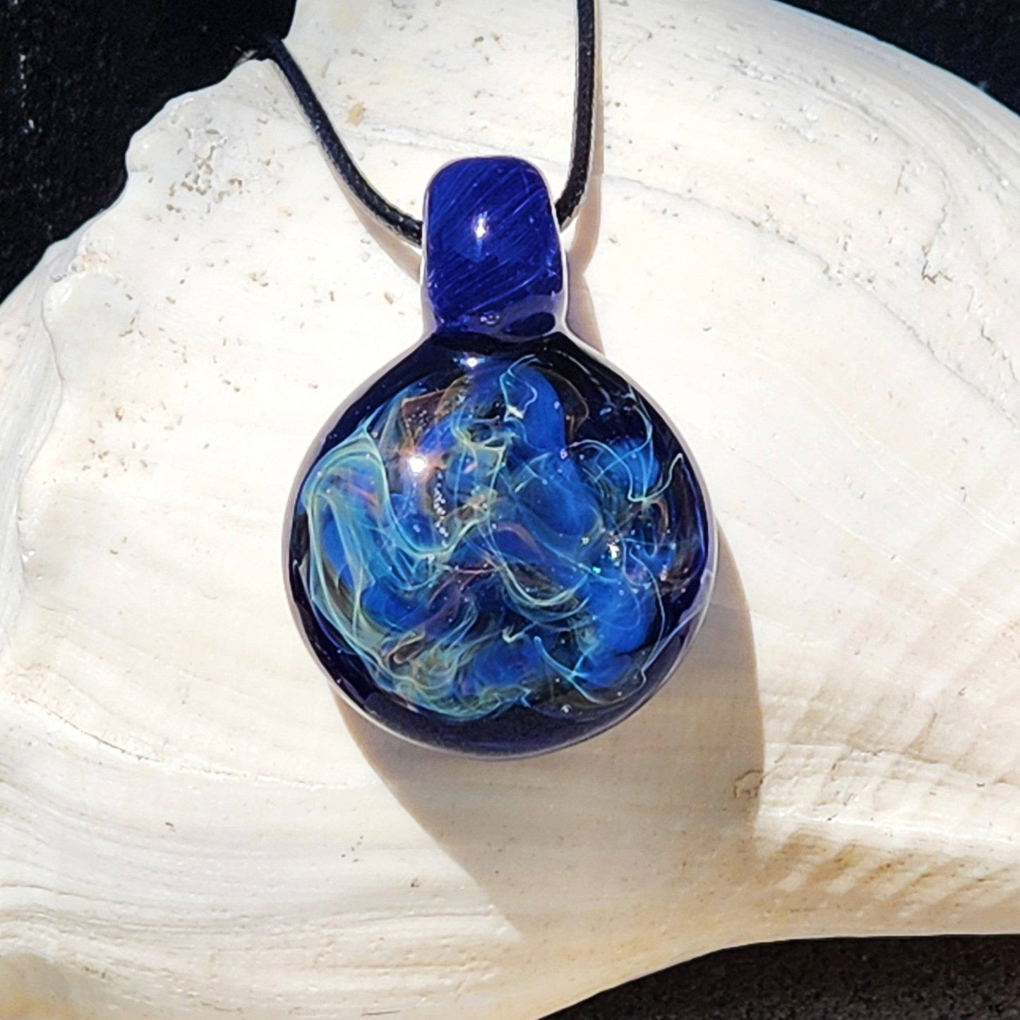 Heady glass pendant necklace with silver and gold fumed blue swirls displayed on a white seashell, perfect for unique jewelry lovers.