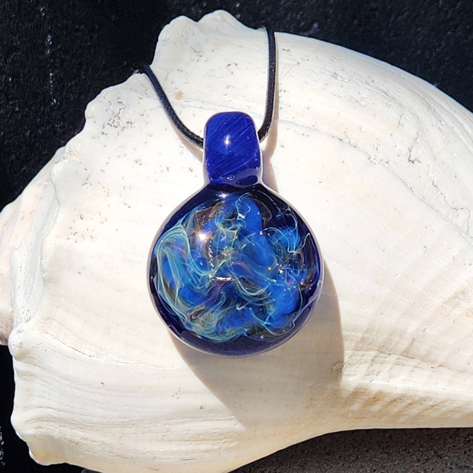 Trippy blown glass pendant featuring pure silver and gold fuming with vibrant blue lines, displayed on a white seashell backdrop.