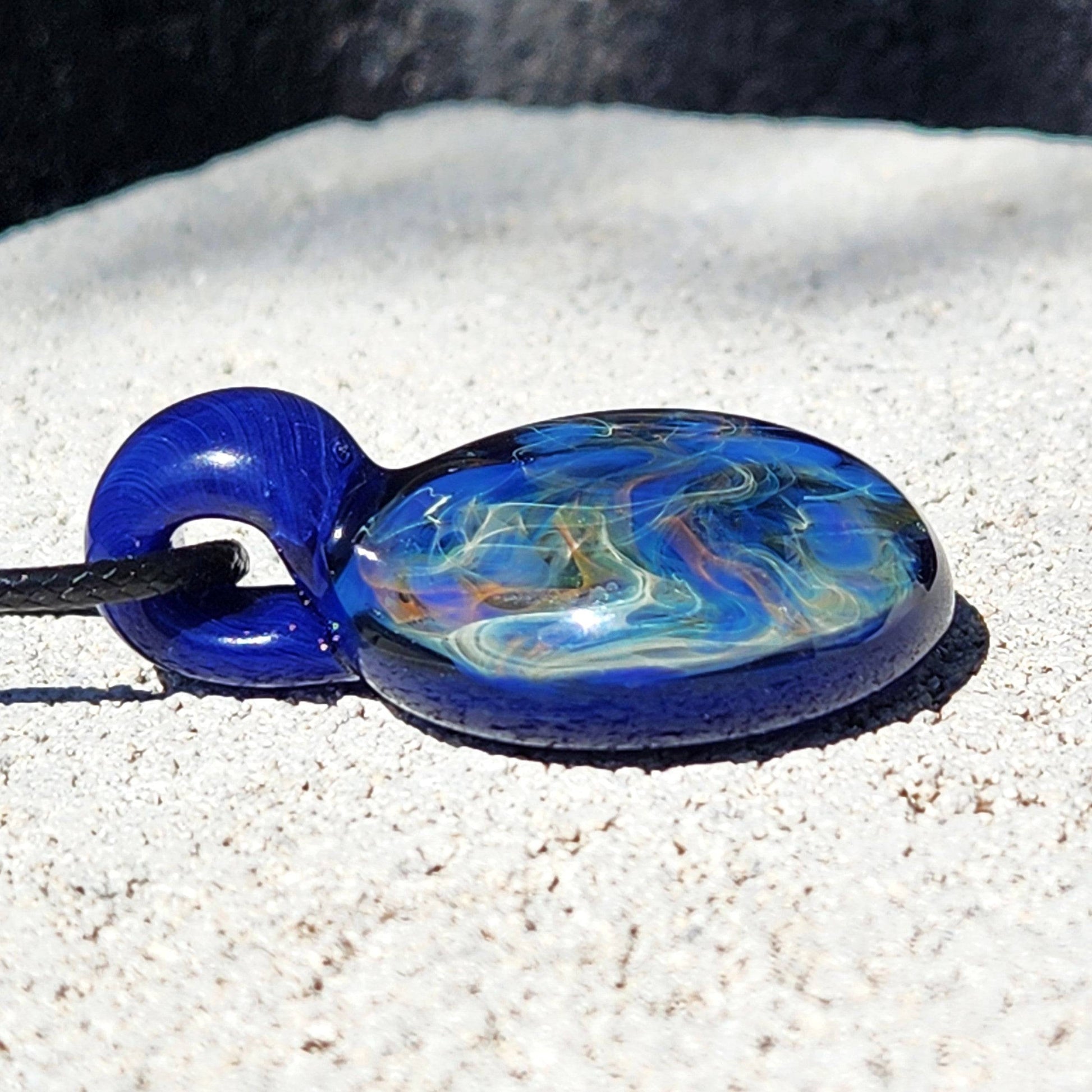 Side view of handmade glass pendant showing layered blue and gold fumed swirls, ideal for artistic jewelry collections.