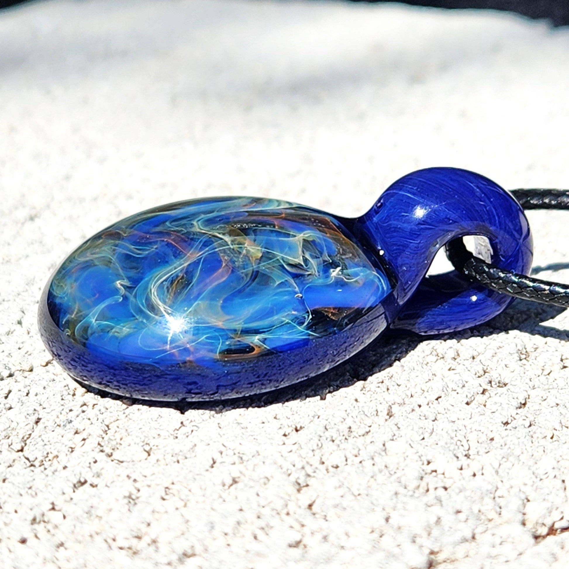 Flat-lay of trippy glass pendant necklace with deep blue base and colorful fumed swirls, ideal for boho or artistic fashion.