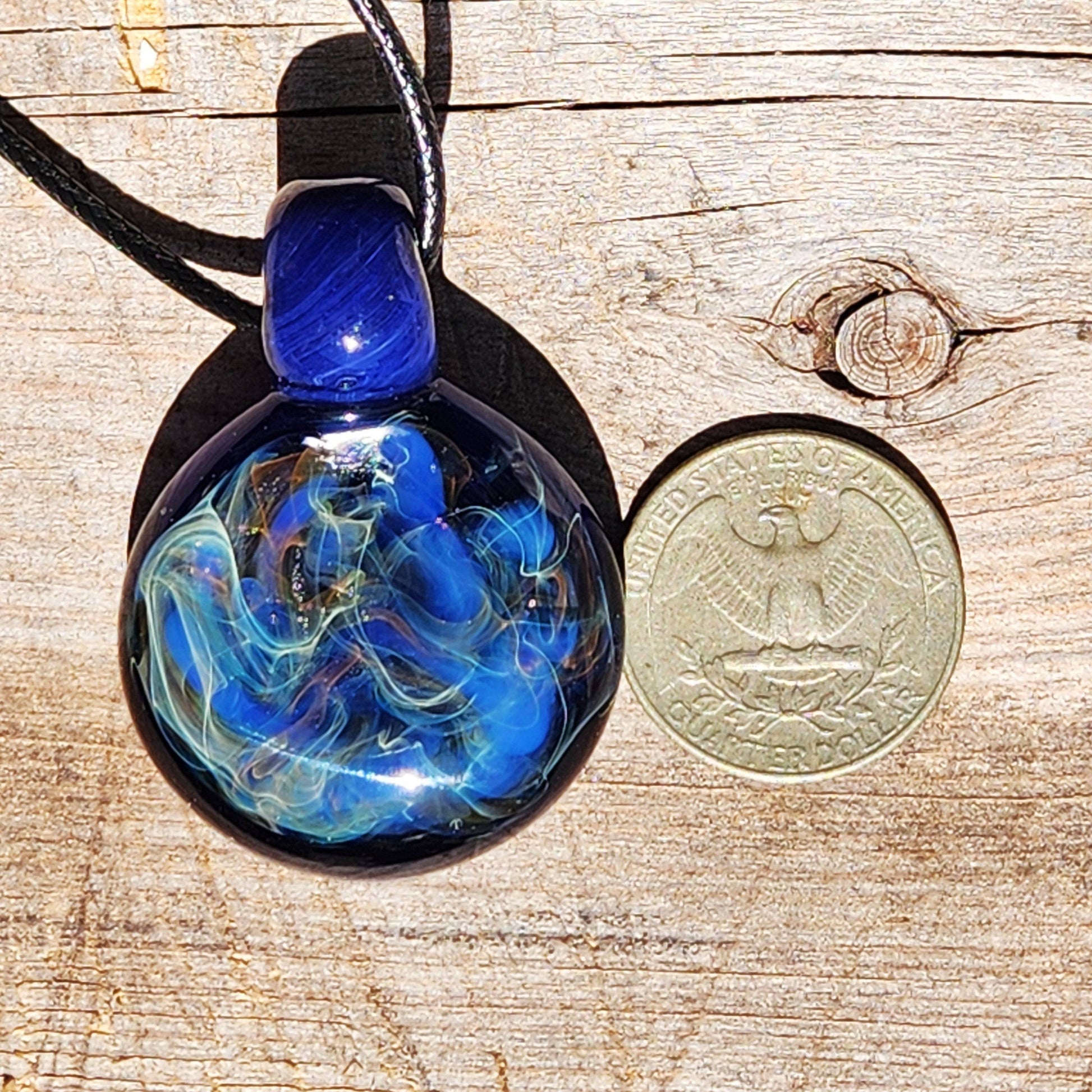Glass pendant necklace with swirling blue, gold, and silver fuming shown next to a U.S. quarter for size comparison.