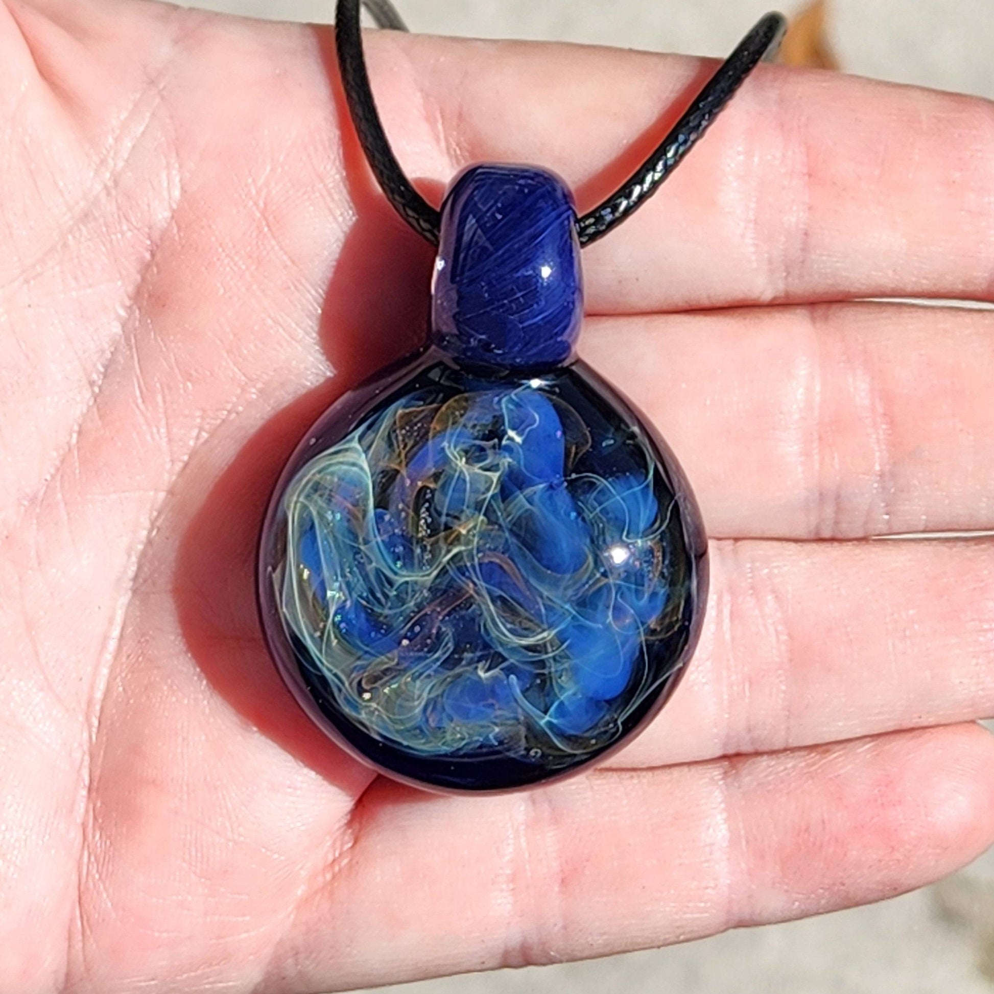 Handmade trippy glass pendant with blue and gold fumed design held in palm, showcasing its artistic craftsmanship.