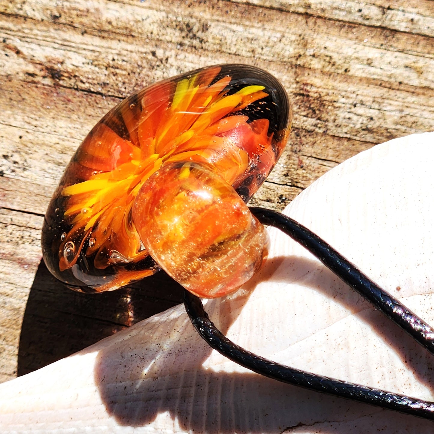 Side view of borosilicate blown glass pendant necklace showing detailed orange and red flower encased in clear glass on wood surface.