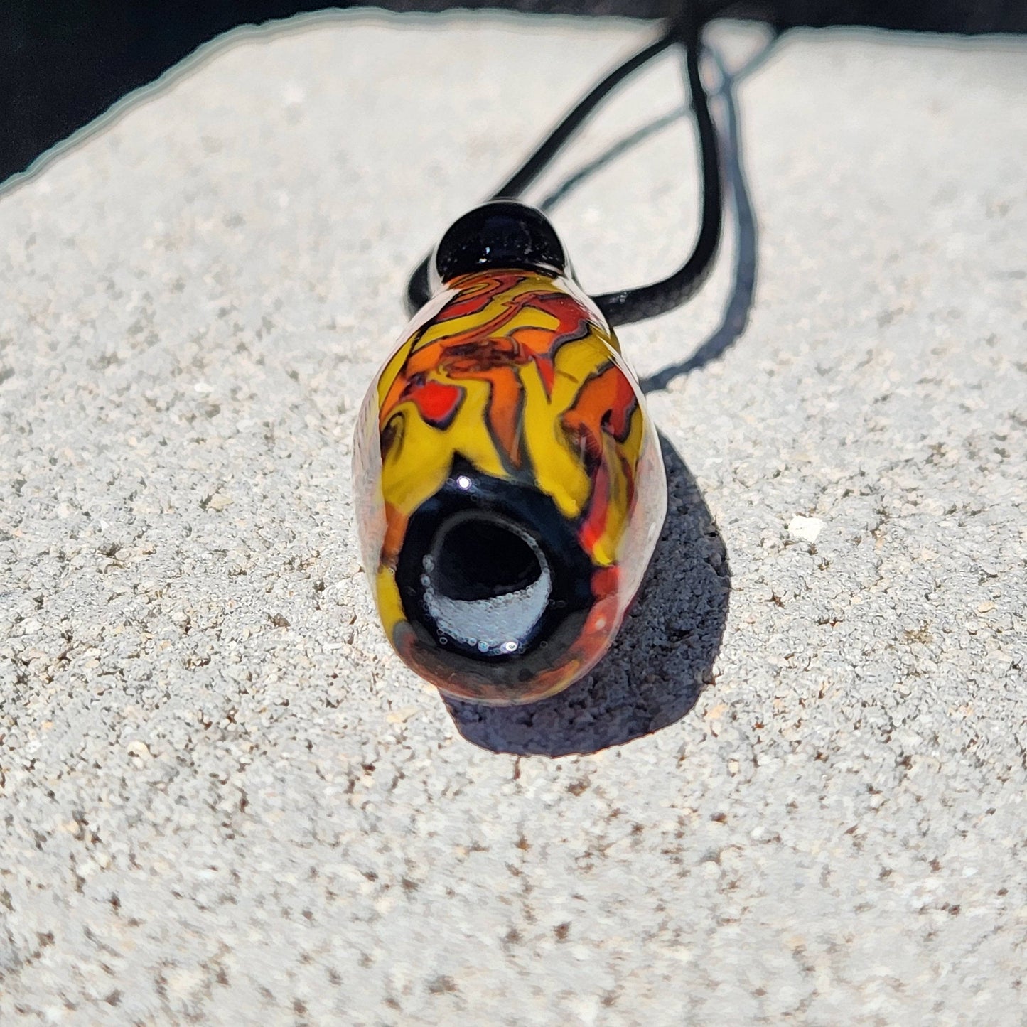 Bottom view of Handblown Tubular Glass Pendant showing hollow black glass tip and vibrant yellow-red swirl design. Unique handmade pendant.