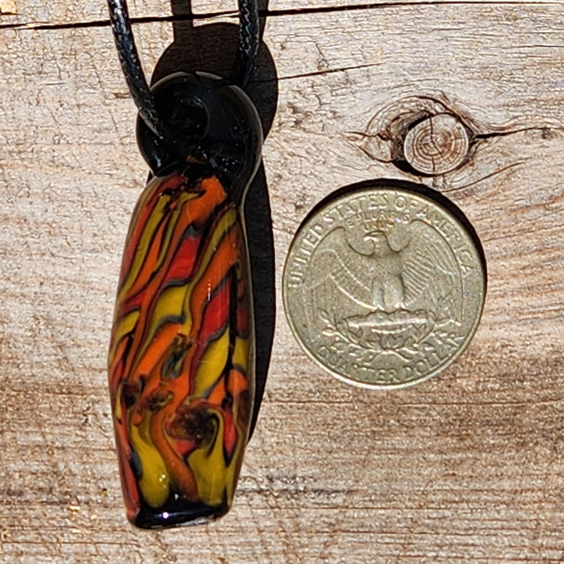 Handblown Tubular Glass Pendant next to a US quarter for size comparison. Features vivid flame colors on black. Unique handmade jewelry charm.