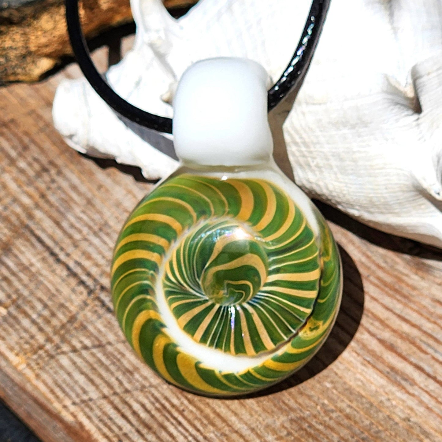 Handmade Spiral Glass Pendant resting on wood with shell, showcasing its vibrant green-yellow swirl and white glass loop.