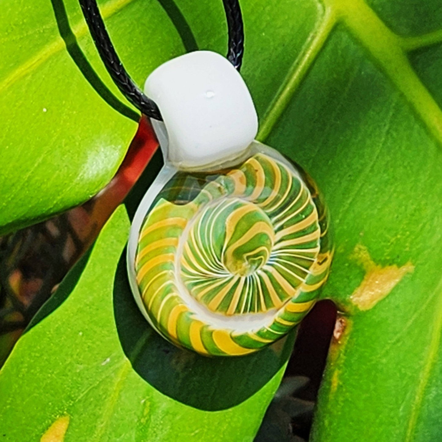 Handmade Spiral Glass Pendant featuring vibrant yellow and green spiral design, shown on a leaf. Unique borosilicate glass necklace.